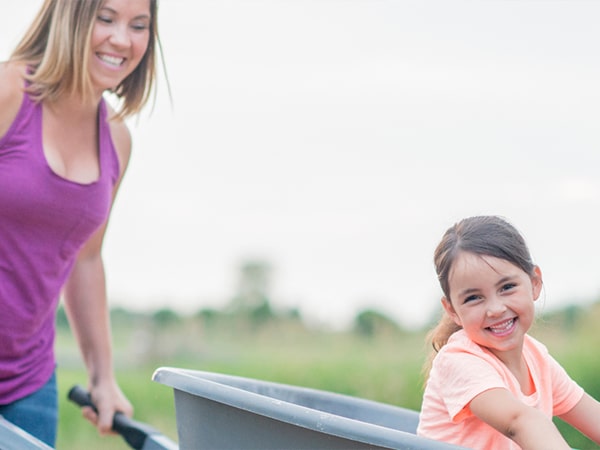 woman pushing her daughter inside a wheelbarrow
