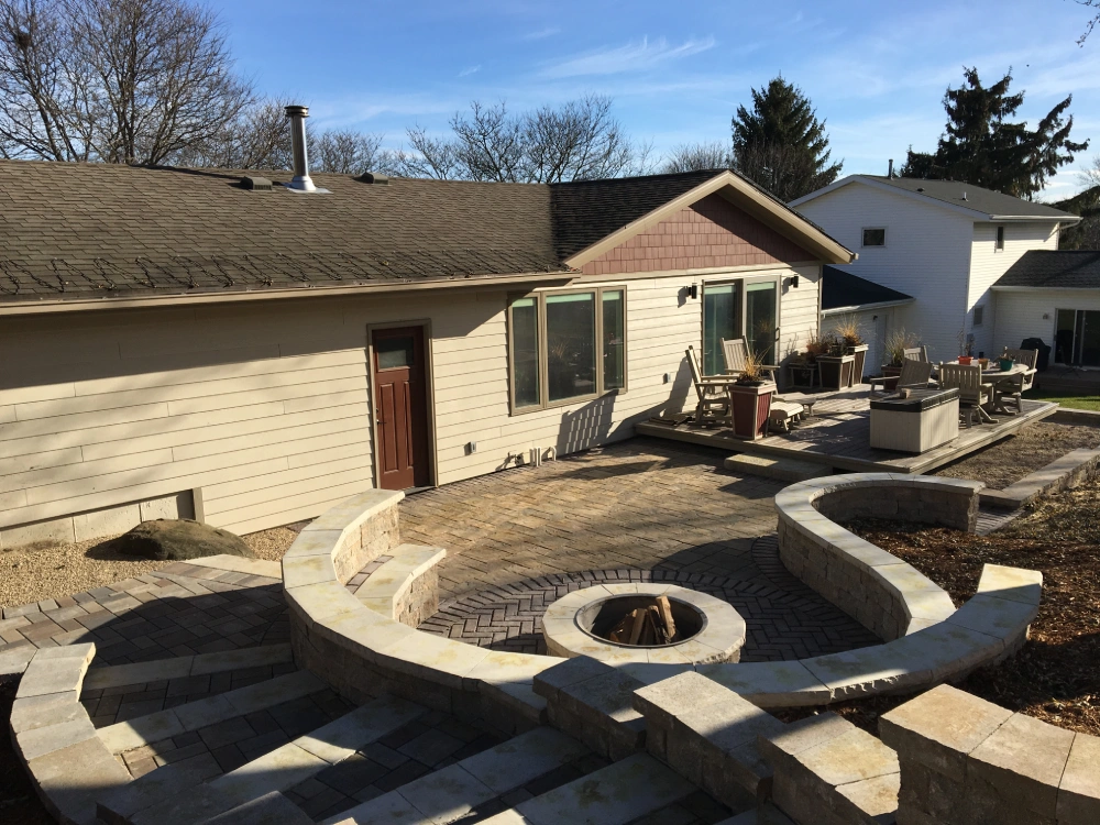 Newly renovated backyard featuring a stone patio, integrated fire pit, and seating wall as part of a comprehensive outdoor transformation by Carrington Lawn Landscape