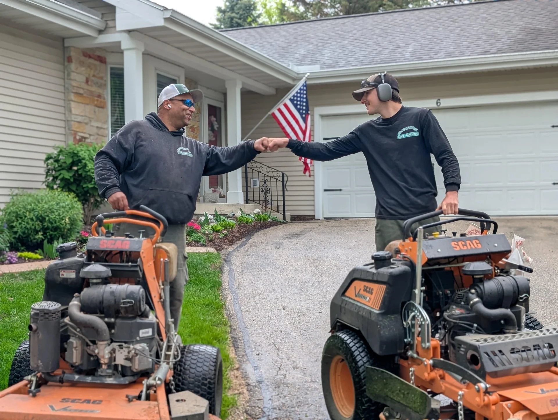 Carrington Lawn Landscape lawn care team members collaborating and fist bumping next to professional mowing equipment during residential service