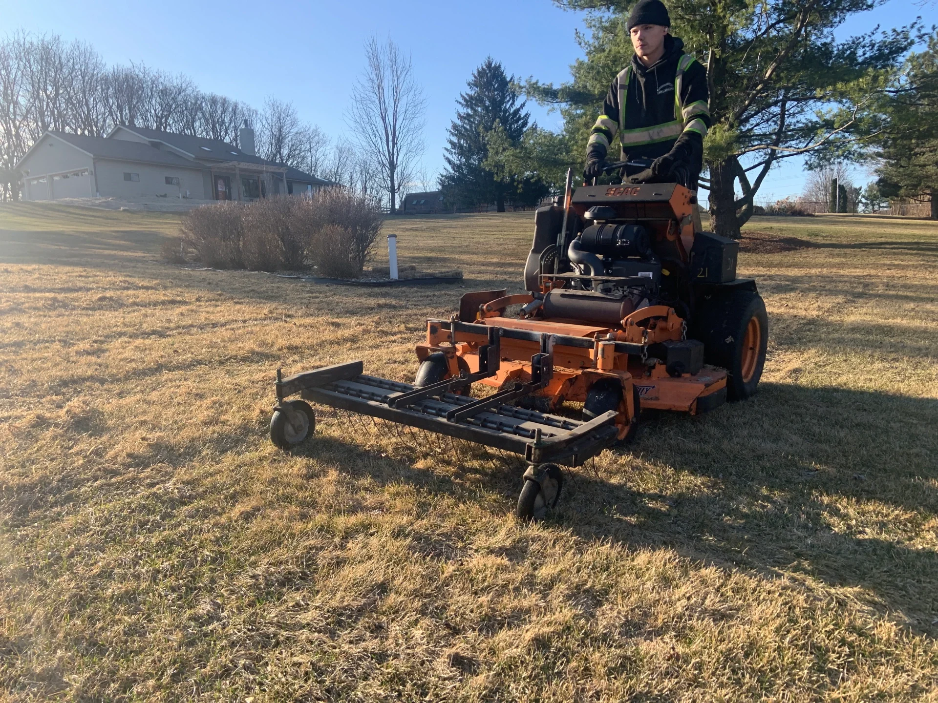 Technician performing spring lawn dethatching and debris cleanup with professional equipment by Carrington Lawn Landscape