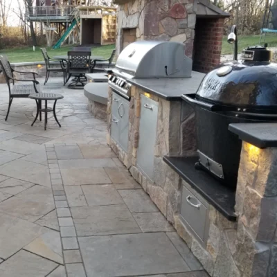 Spacious stone outdoor kitchen with built-in grill, smoker, and adjacent dining area by Carrington Lawn & Landscape in Madison