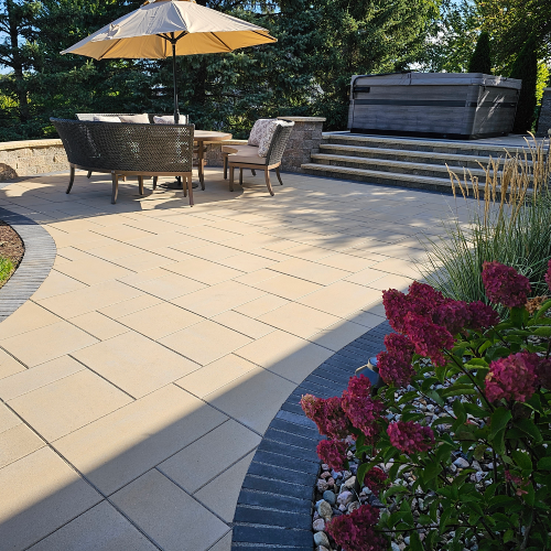 Spacious multi level paver patio with outdoor dining set, umbrella, hot tub, and landscaped flower bed in Wisconsin