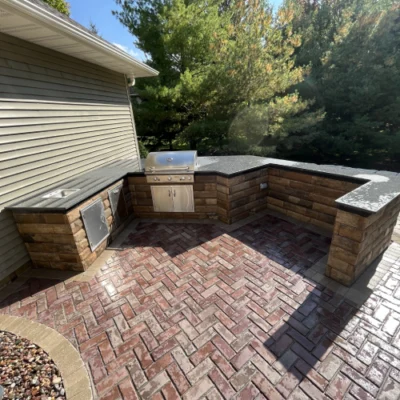 Outdoor kitchen featuring L-shaped layout, stone surfaces, and herringbone brick patio for outdoor kitchen planning by Carrington Lawn & Landscape in Madison