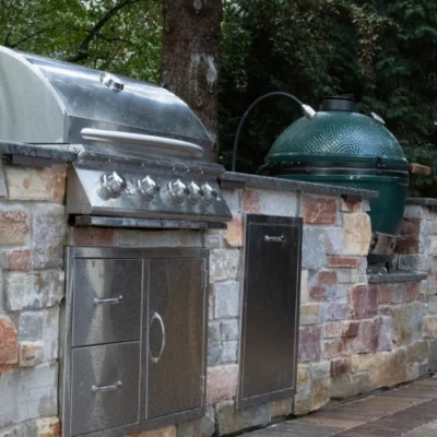 Close-up of outdoor kitchen showcasing built-in stainless grill, Green Egg ceramic cooker, and stonework by Carrington Lawn & Landscape in Madison