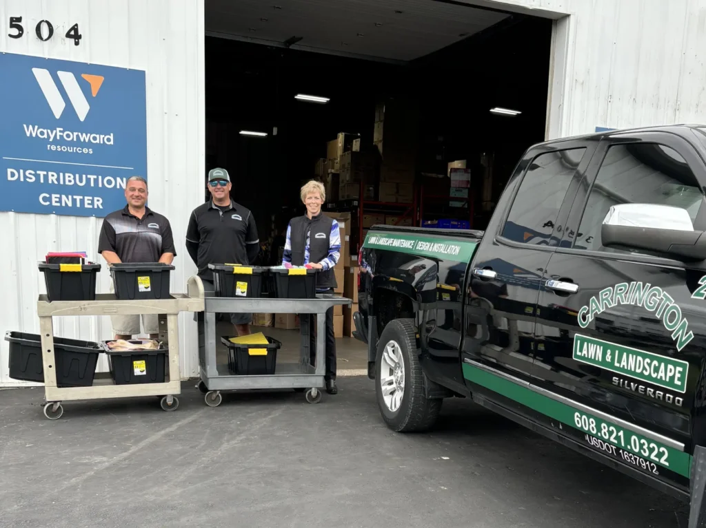 Three Carrington Lawn & Landscape employees and a branded company truck outside a distribution center in Madison, loading donation supplies