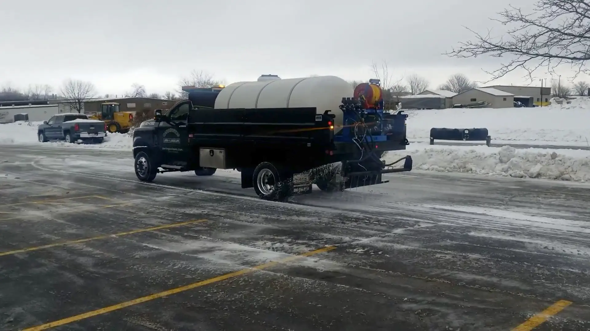 Medium-duty truck with a large brine tank sprays anti-ice across parking lanes during a commercial snow removal service by Carrington Lawn & Landscape in Middleton, Madison, and the greater Dane County area