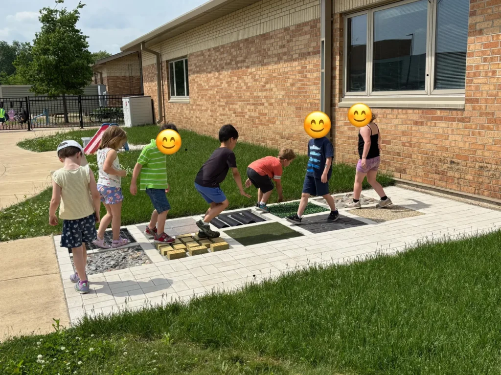Young children walking and playing on outdoor sensory pathway tiles installed by Carrington Lawn & Landscape at a school in Madison