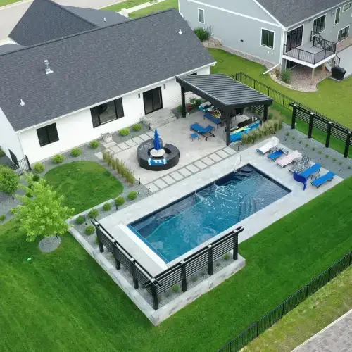 Modern outdoor living space with a swimming pool, pergola, lounge area, and lush green lawn designed by Carrington Lawn & Landscape in Middleton, WI.