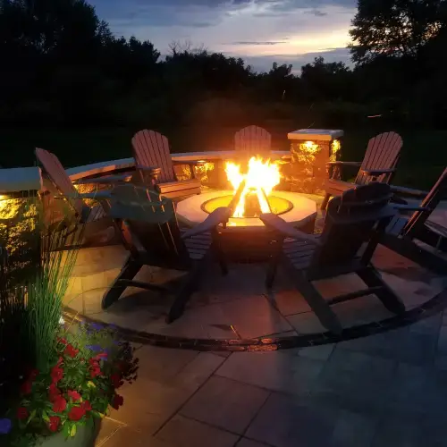 Modern fire pit landscape design trends featuring a round stone fire pit and Adirondack chairs in a beautifully landscaped backyard at dusk in Middleton, WI