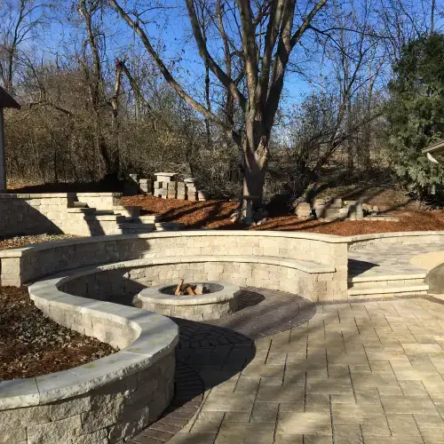 Curved stone patio with built-in seating and a central fire pit showcasing landscape design trends in Middleton, WI