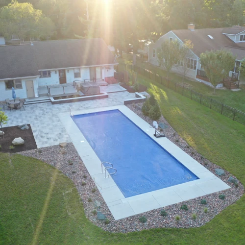 Backyard poolside landscape project with modern pool and sunlit yard by Carrington Lawn & Landscape in Monona, WI