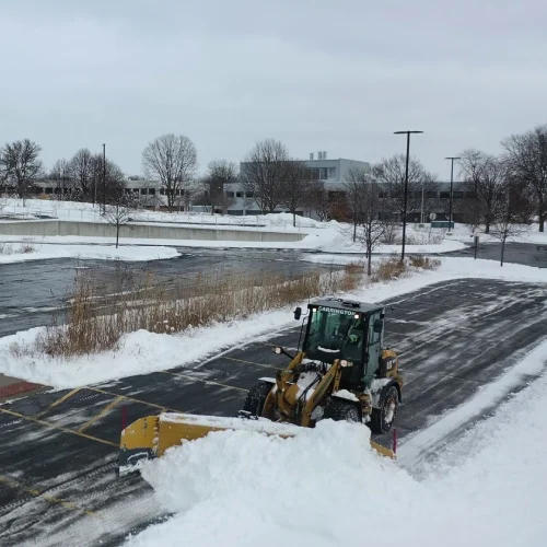 Loader with snow pusher clearing lanes in a commercial parking lot, certified snow professional service by Carrington Lawn & Landscape