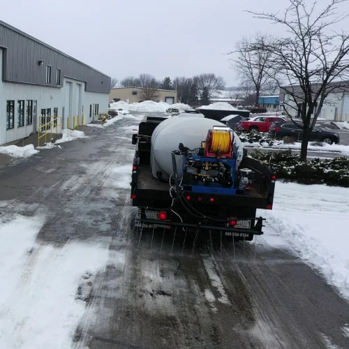 Truck‑mounted tank applies liquid brine to an industrial driveway for anti‑icing, certified snow professional service by Carrington Lawn & Landscape