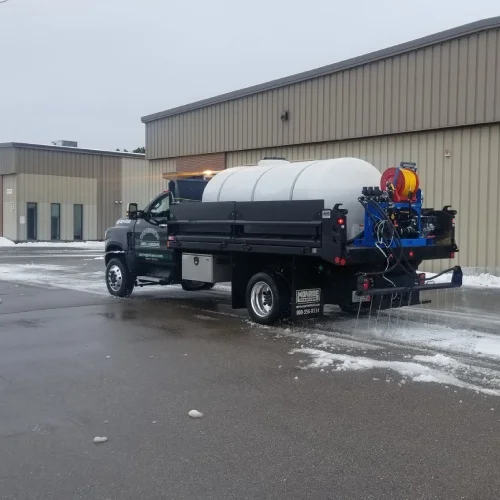Liquid brine de‑icing truck sprays anti‑icing on a commercial lot, demonstrating snow and ice removal technology by Carrington Lawn & Landscape
