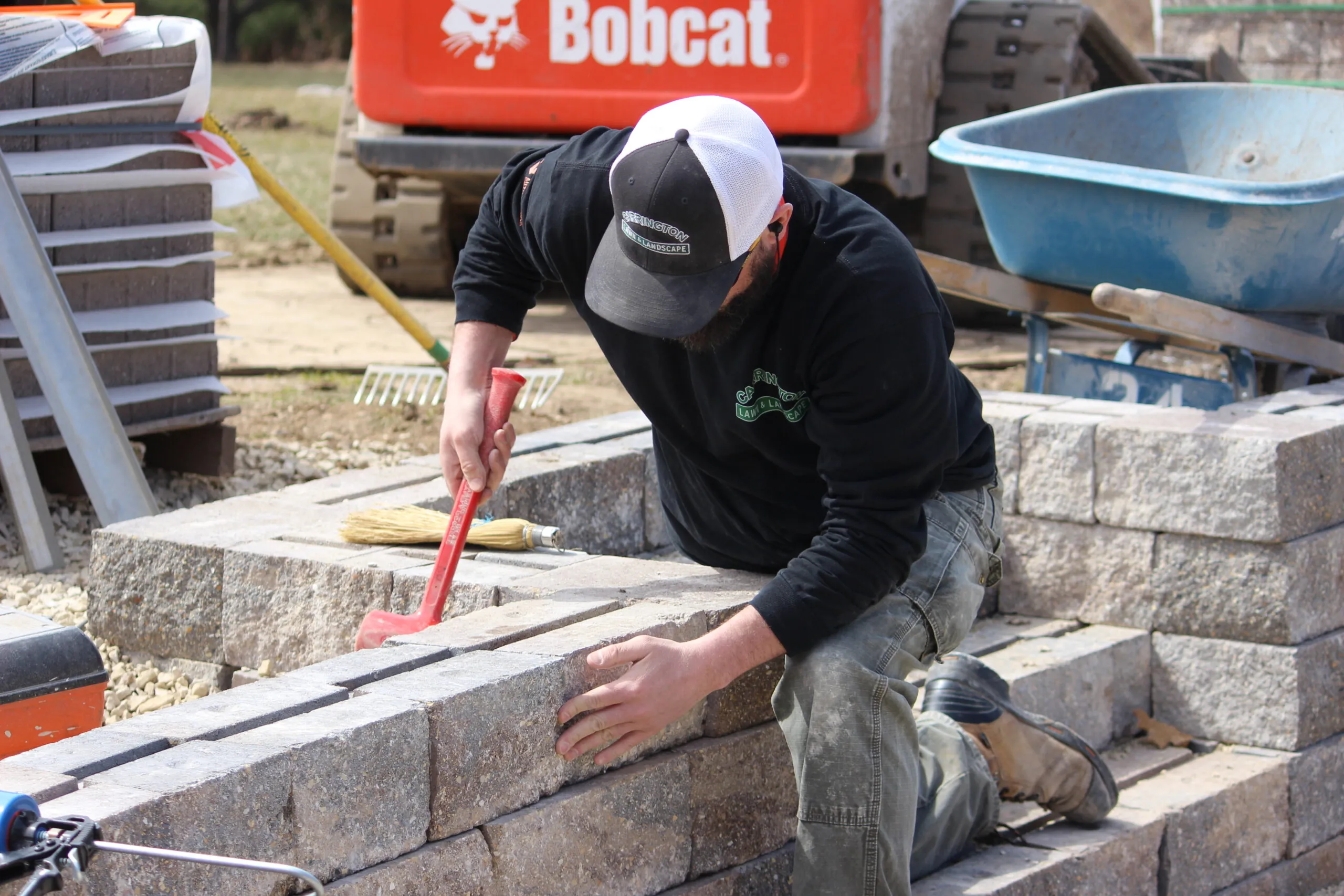 Carrington Lawn & Landscape team member holding equipment installing hardscape bricks in middleton, WI