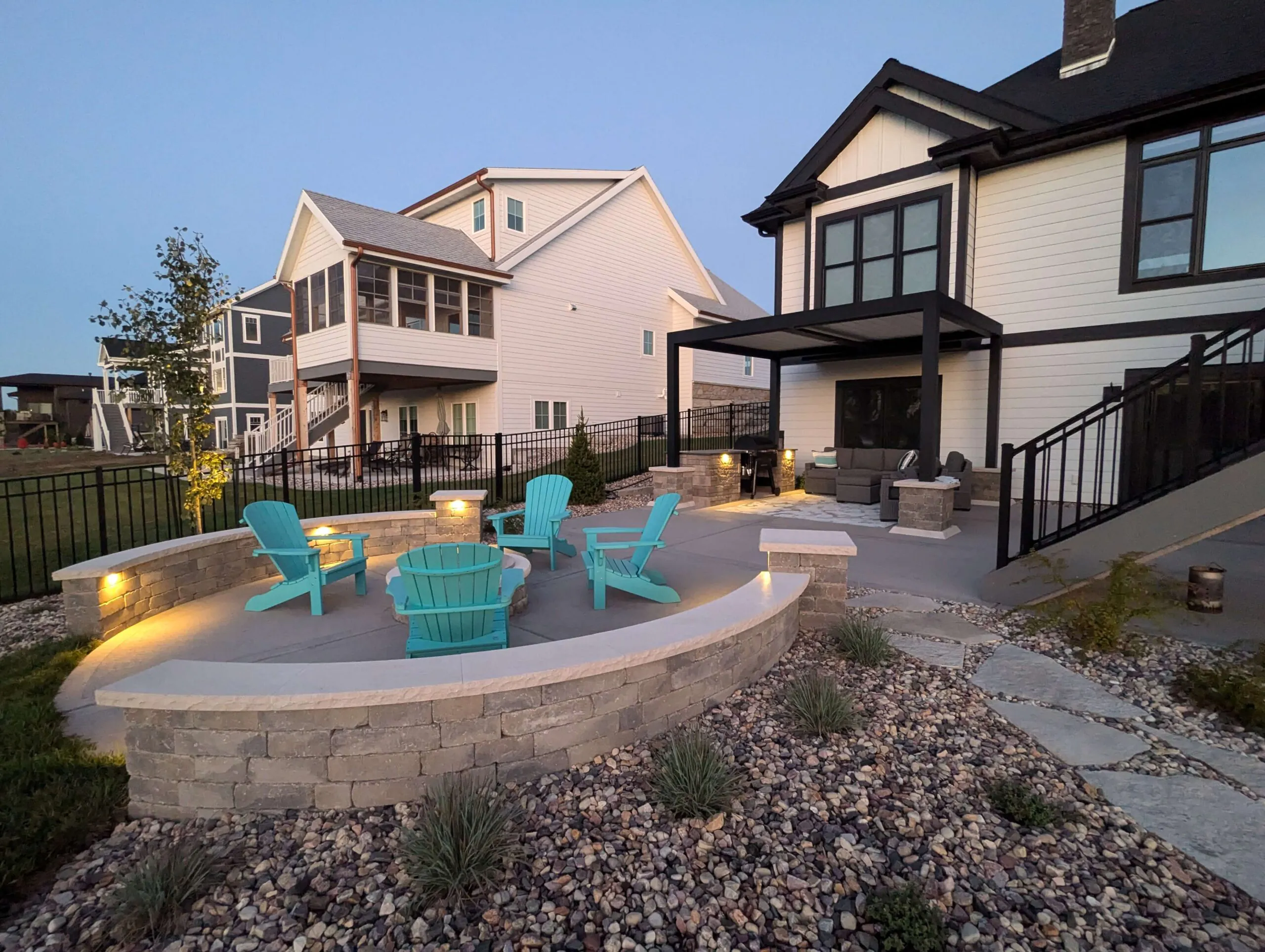 Curved stone patio with integrated seat walls, built-in lighting, and bright blue chairs surrounding a fire pit, showing patio paver designs in Middleton, Wisconsin by Carrington Lawn & Landscape