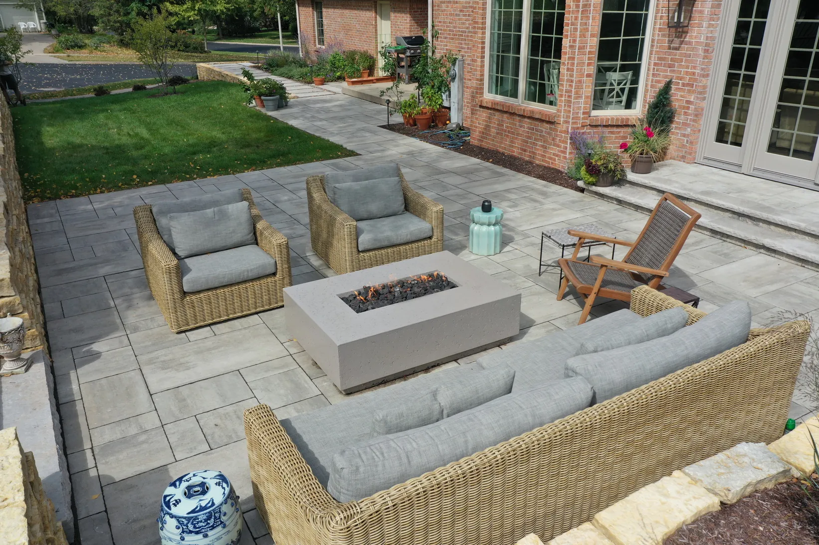 Large ashlar pattern paver patio with a rectangular gas fire table and outdoor wicker seating, highlighting patio paver designs in Middleton, Wisconsin by Carrington Lawn & Landscape