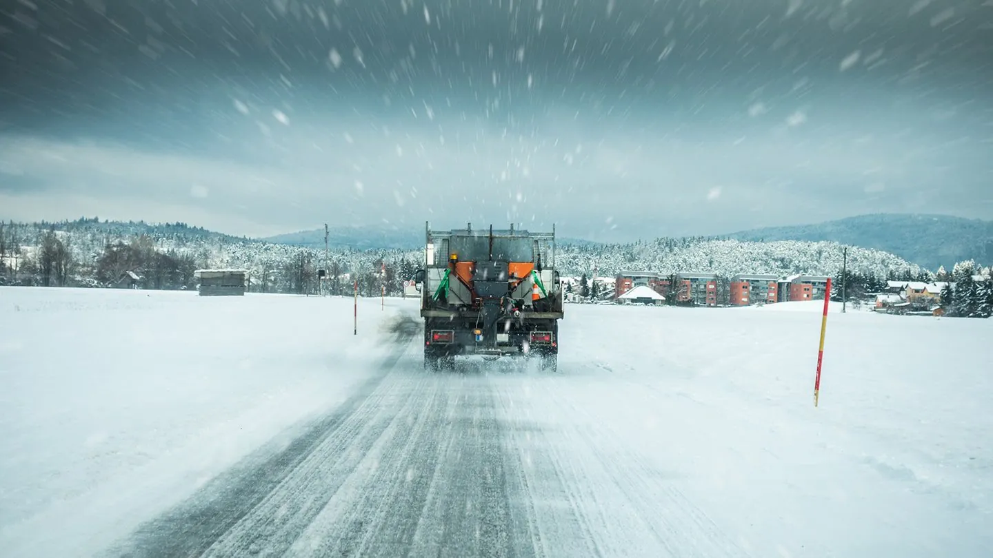 Rear view of a sone and ice management snowplow truck driving on a snowy road during a snowstorm in Madison, WI