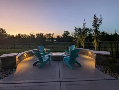 A curved stone fire pit seating area at sunset showing a DeForest patio and fire pit project in Middleton by Carrington Lawn & Landscape.