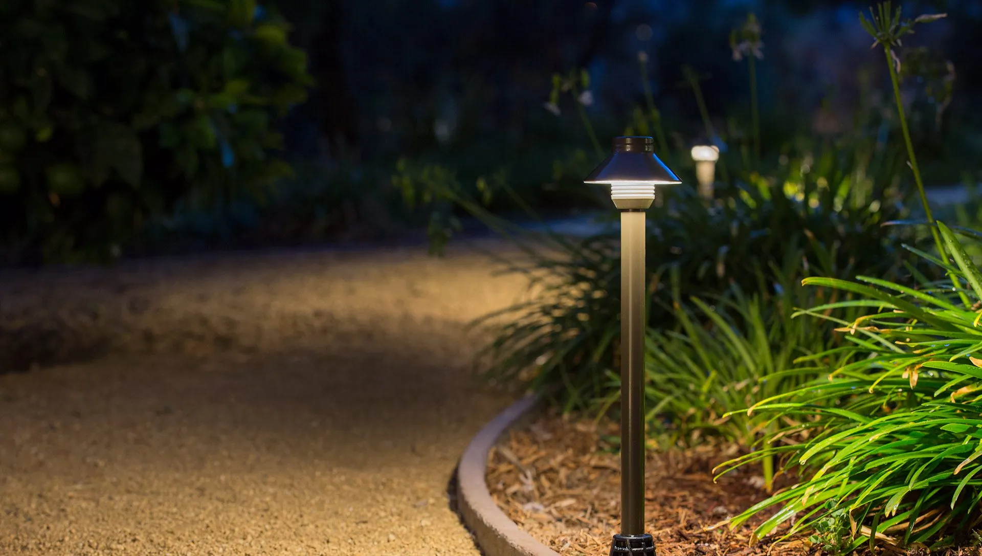 A low-angle shot of a dimly lit landscape lighting design pathway in a garden at dusk in Middleton, WI