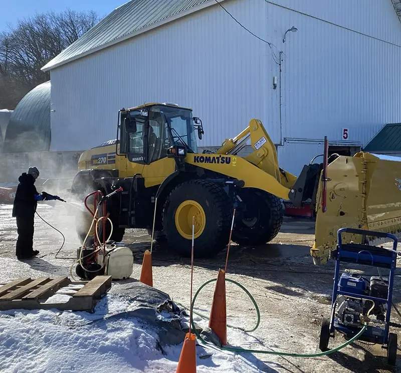 A Carrington Lawn & Landscape crew member uses a pressure washer to clean a komatsu commercial snow and ice management mobile equipment in Madison, WI