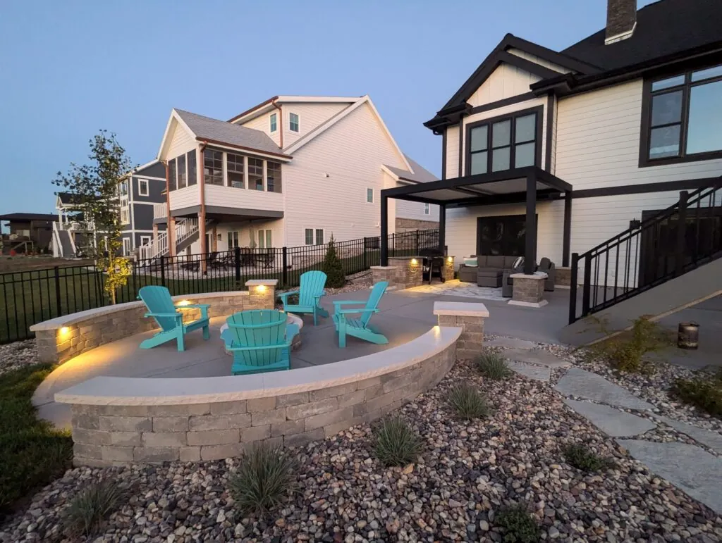 A modern patio with a circular fire pit, Adirondack chairs, and a curved seating wall with accent lighting in Middleton, WI