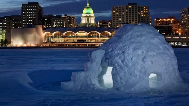 An igloo on a frozen lake at night and a commercial building in the background in Madison, WI