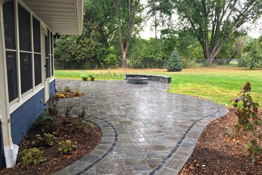 A backyard hardscape design patio with a fire pit, curved seating wall, and a variety of plants and shrubs