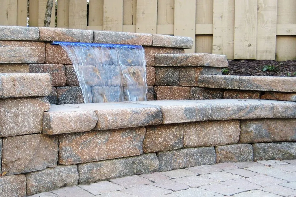 A hardscape design tiered stone retaining wall with a small, sheet-like waterfall flowing in Middleton, WI