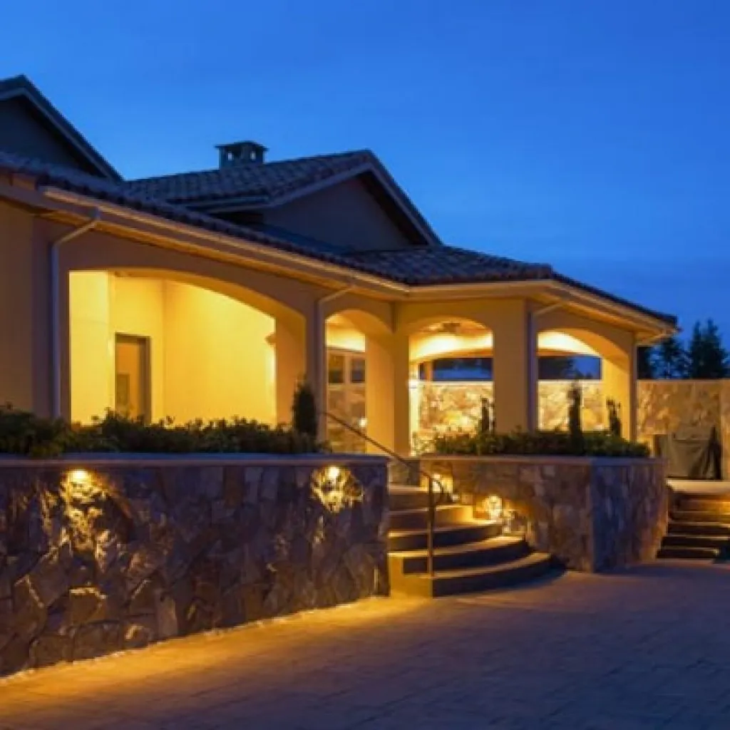 A large house with a patio and stone retaining wall illuminated by various landscape lighting design fixtures at night in Middleton, WI
