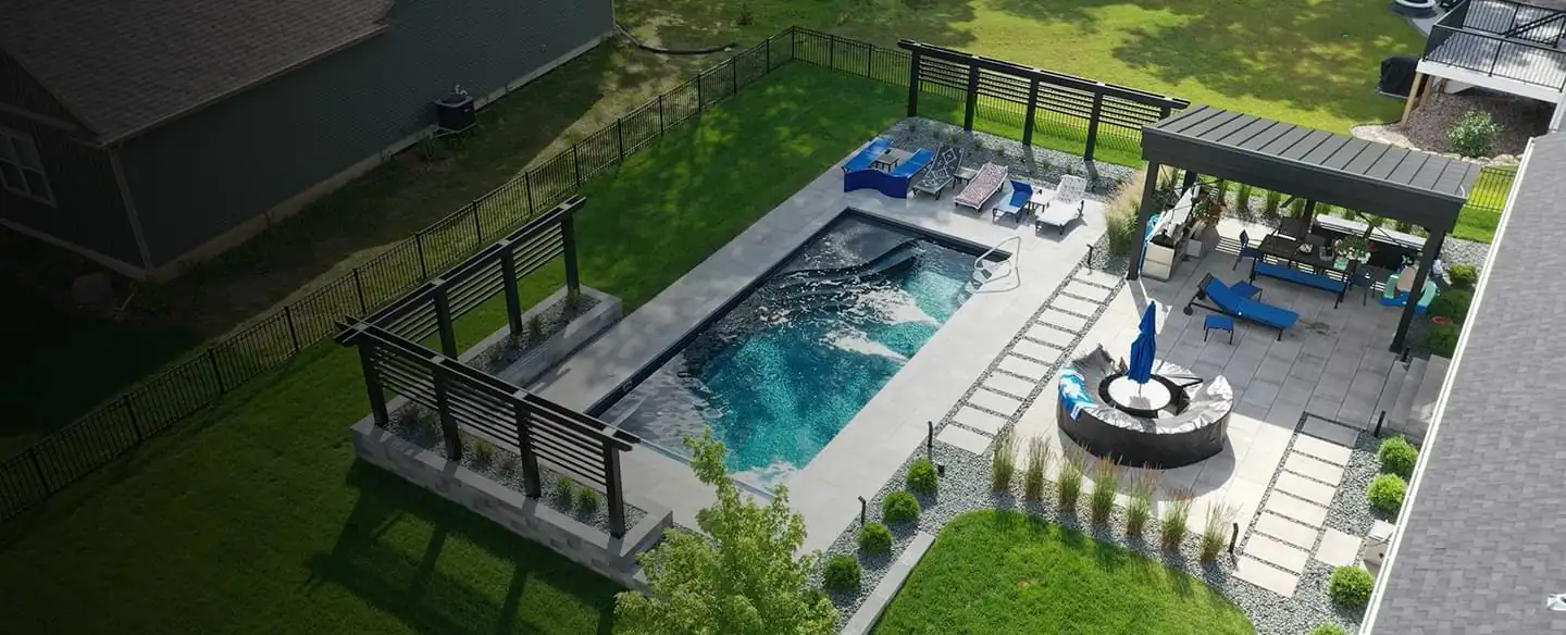 Aerial view of a modern backyard featuring a sleek rectangular swimming pool, a covered patio with lounge seating by Carrinton Lawn & Landscape softscape landscaping services in Middleton, WI
