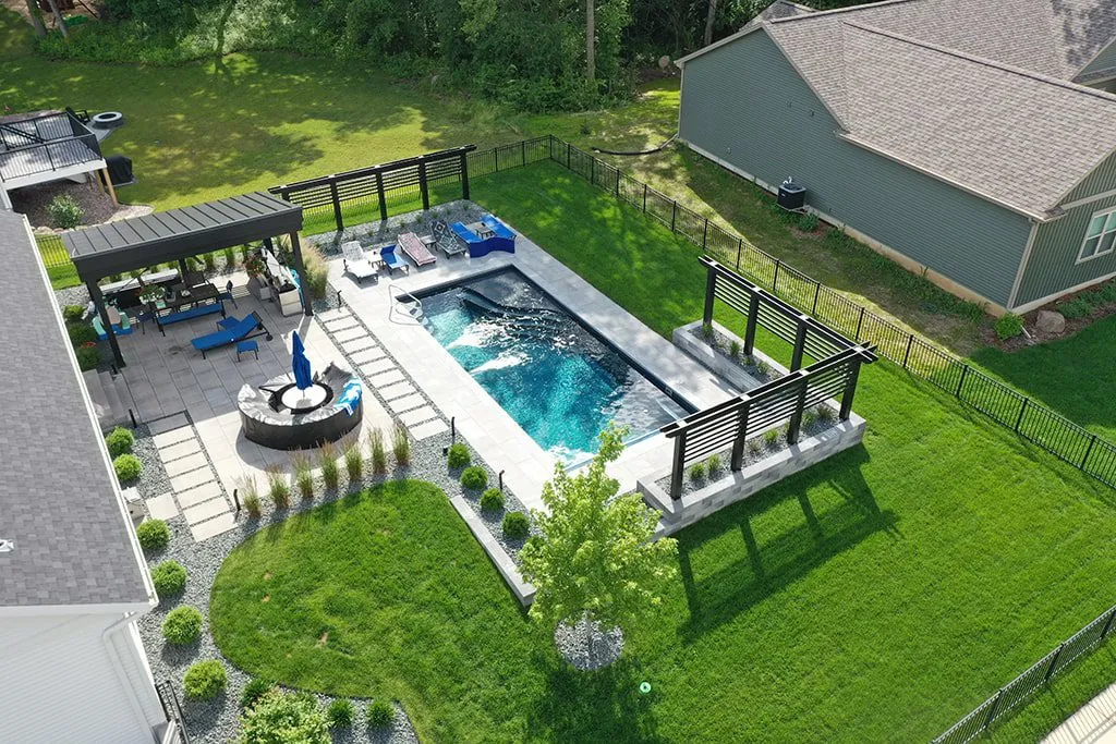 Drone shot of a backyard with a rectangular pool, patio with pergola, and landscaped areas in Middleton, WI