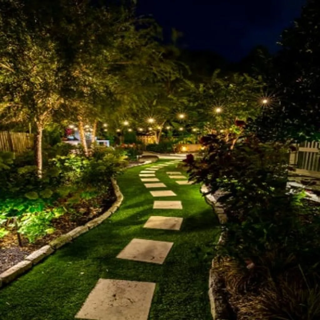 A winding path with stepping stones and string lights illuminated by landscape lighting lighting in a backyard garden at night in Middleton, WI
