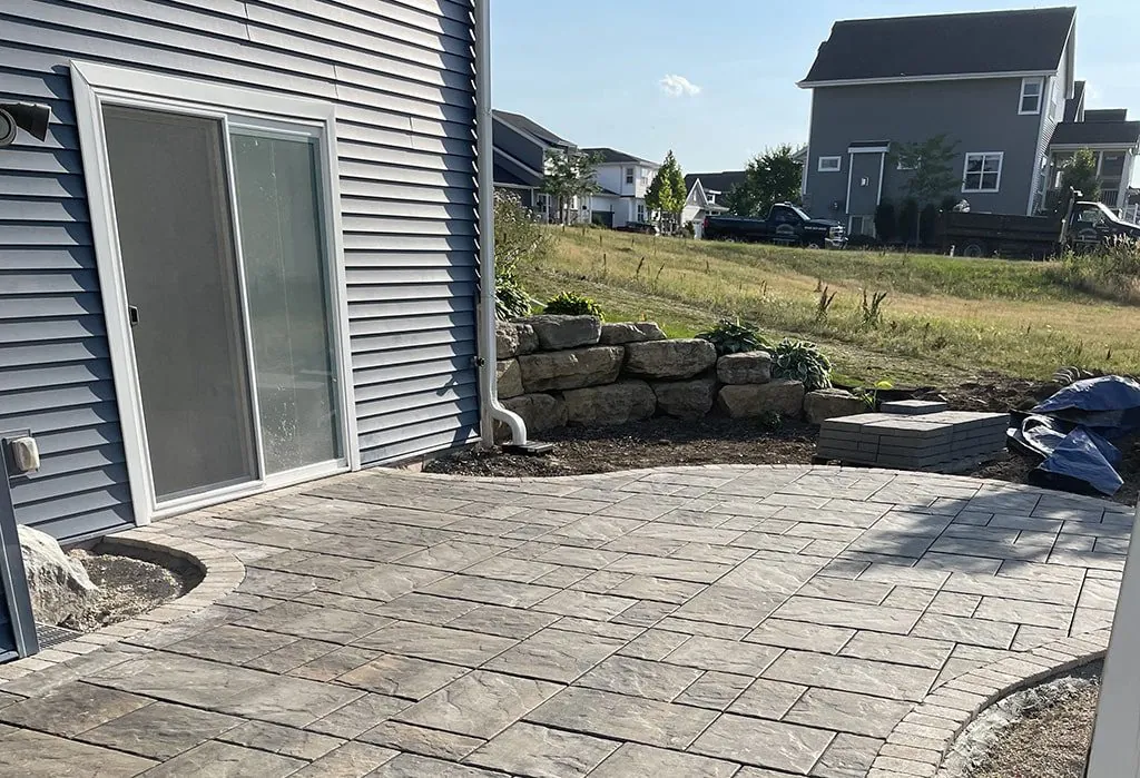 Light gray paver patio with a sliding glass door and stone retaining wall in Middleton, WI