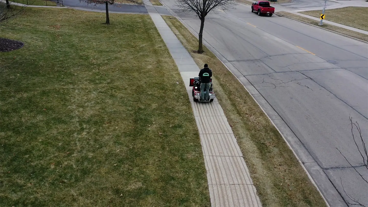 Worker using a de-icing machine on a sidewalk as part of a snow and ice management service in Madison, WI