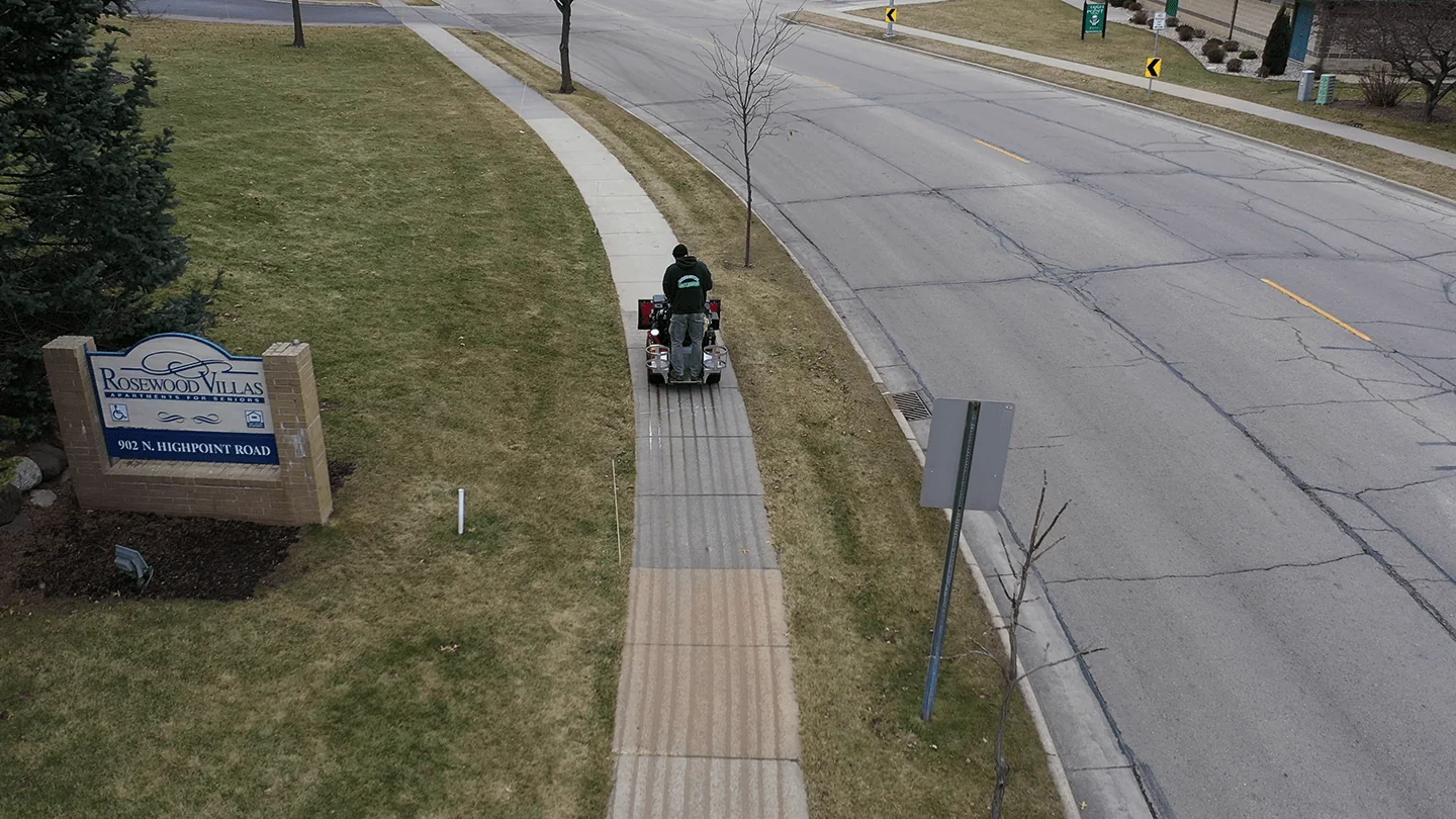 Worker using a de-icing machine on a sidewalk as part of a snow and ice management service in Madison, WI