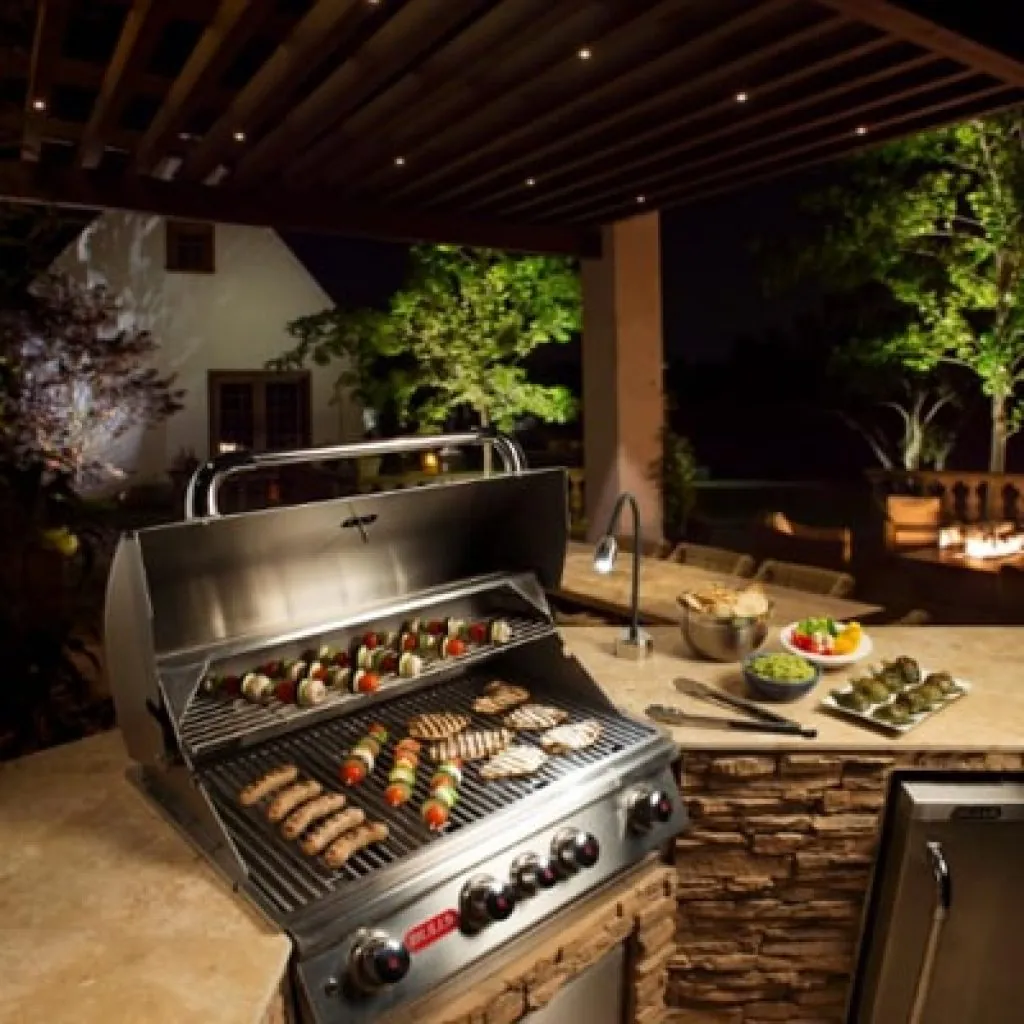 An outdoor kitchen with a built-in grill cooking various meats and vegetables