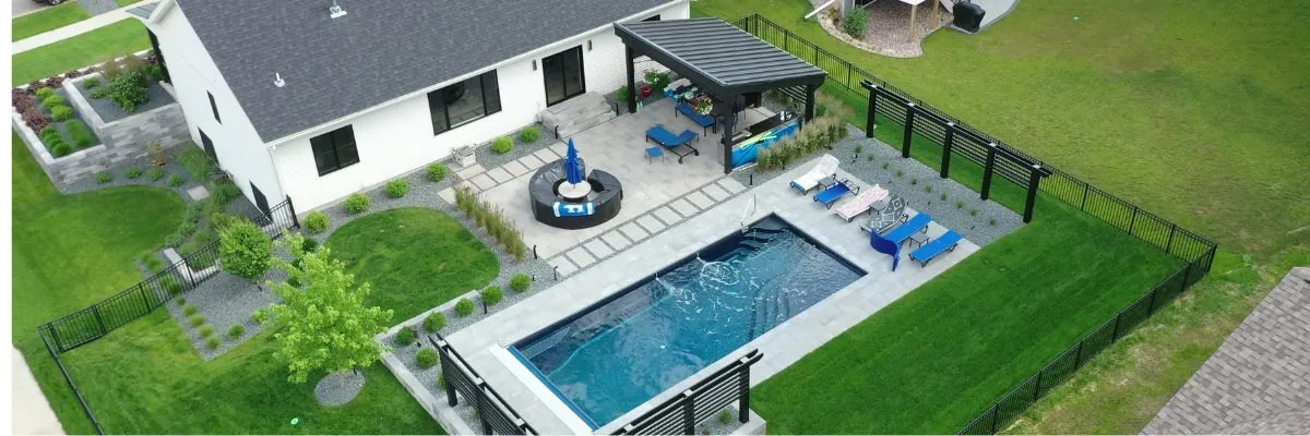 Aerial view of a modern white house with a backyard featuring a rectangular pool, a gray patio with a pergola by Carrington Lawn & Landscape Landscape Design Build contractors in Middleton, WI