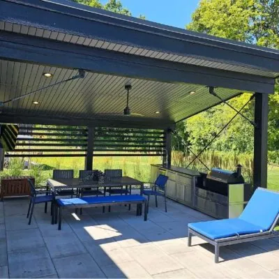 Uutdoor living space with a covered patio, dining table, kitchen island, grill, and lounge chair for landscape design build by Carrington Lawn & Landscape in Middleton, WI
