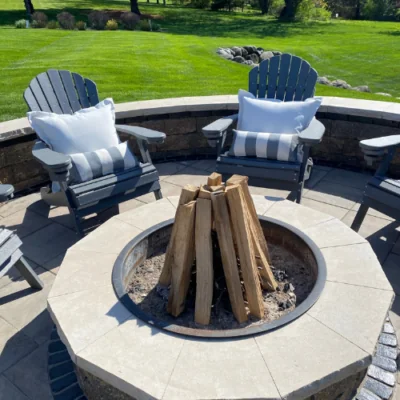 Outdoor patio arrangement featuring a circular fire pit with firewood, surrounded by chairs