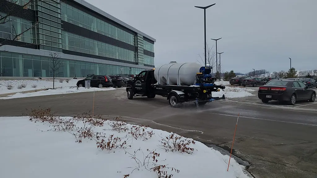 Carrington Lawn & Landscape truck spraying de-icing liquid on a snowy parking lot for snow and ice management in Madison, WI