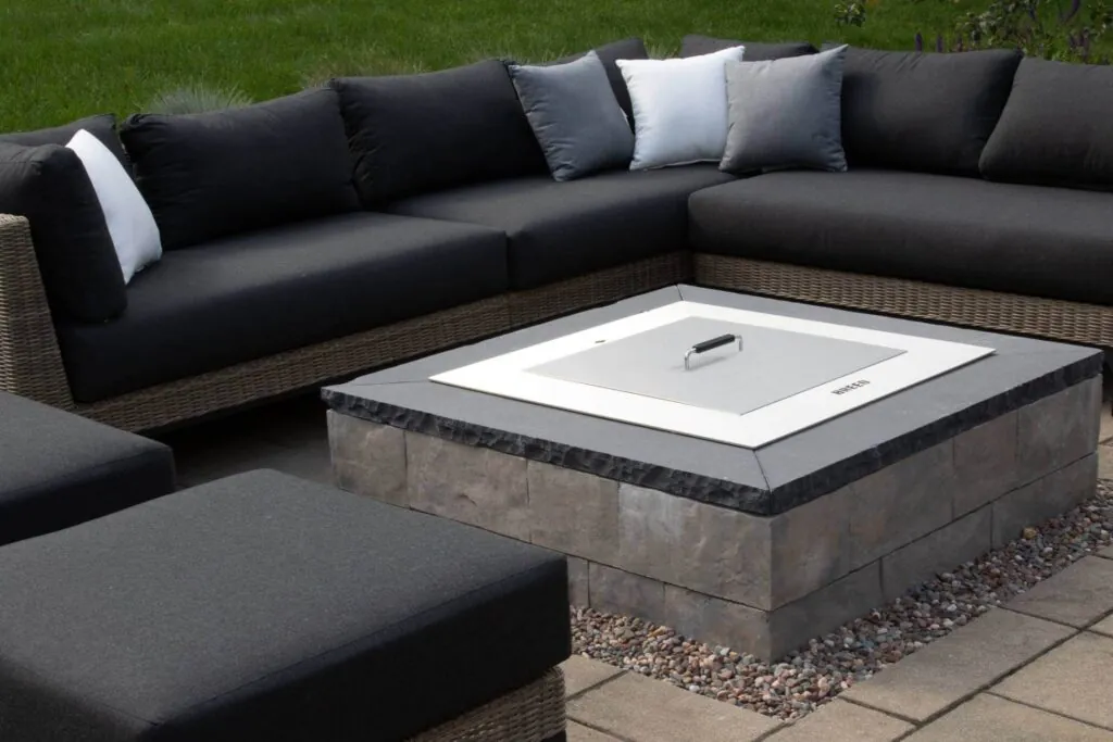 A dark gray sofa with cushions and a square fire pit table on a patio for hardscape design in middleton, WI