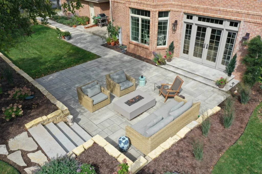 Aerial view of a backyard featuring a large paver patio with a seating area, fire pit, and steps leading to a lower level in middleton, WI