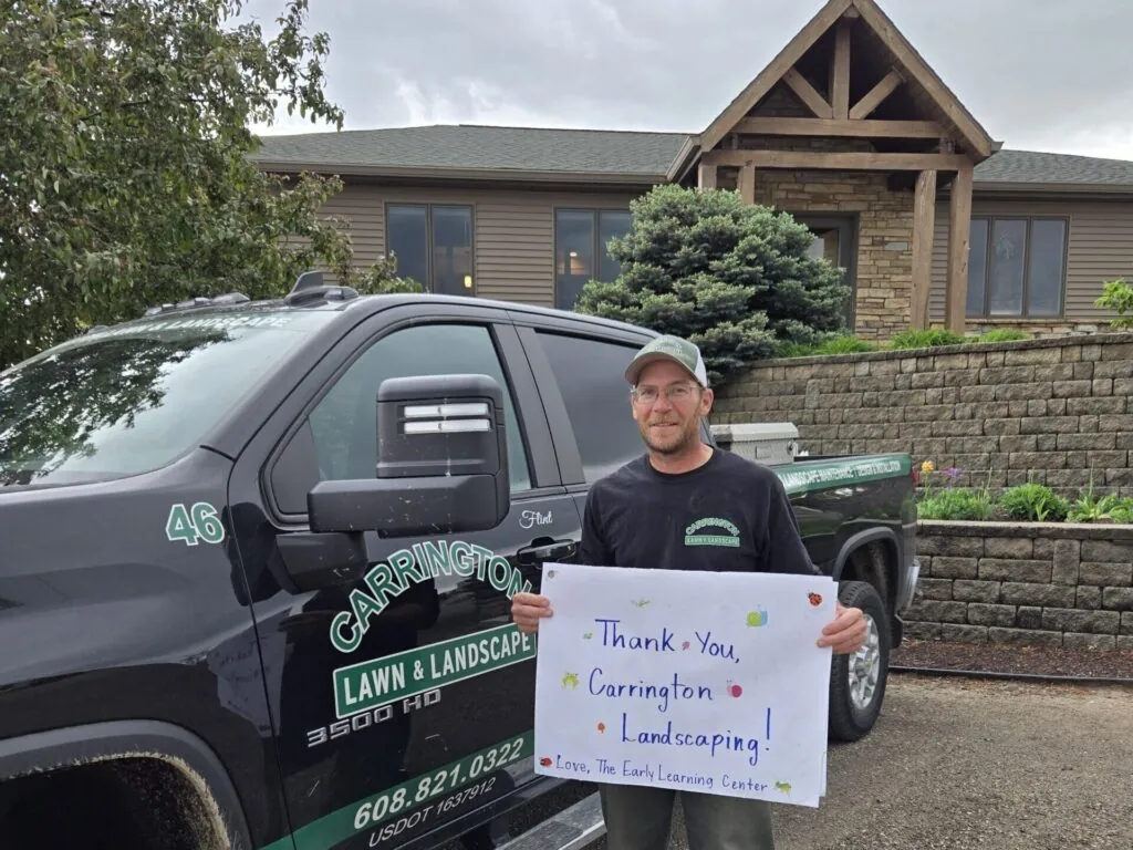 A Carrington Lawn & Landscape employee holding a thank you sign while standing in front of a company truck