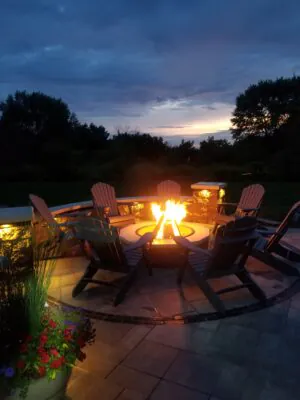 A circular backyard fire pit with surrounding lounge chairs at dusk, showing fire pit design ideas 2026 and fire pit renovation ideas in Middleton by Carrington Lawn & Landscape.