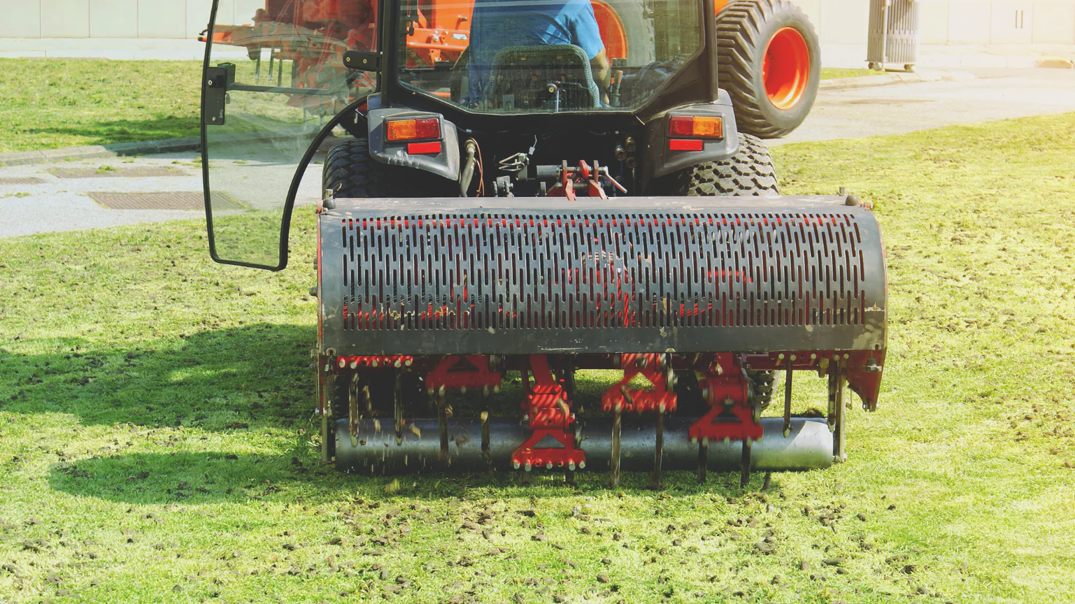 A close-up rear view of a commercial tractor attachment pulling up soil plugs across a green lawn to demonstrate lawn aeration Wisconsin when optimizing grass growth, completed as a lawn aeration service in Middleton, Wisconsin by Carrington Lawn & Landscape.