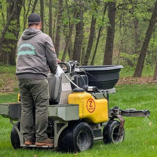 Technician applying fertilizer with a ride-on spreader, organic vs hybrid lawn care fertilization in Madison, WI by Carrington Lawn & Landscape
